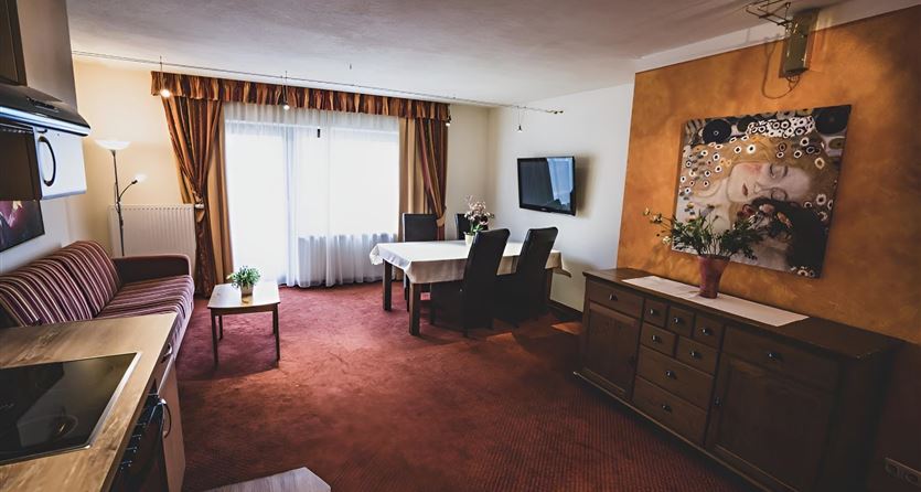 Een gezellige woonkamer met een eettafel en stoelen. De muren zijn in warme kleuren ingericht en er is een kleine keuken en een tv-apparaat.