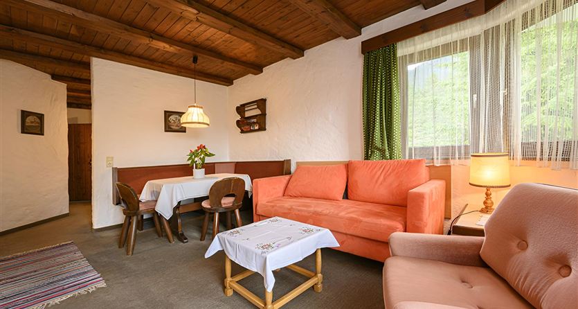 Un accogliente soggiorno con un divano arancione e un tavolo da pranzo. Grandi finestre lasciano entrare molta luce e creano un'atmosfera invitante.