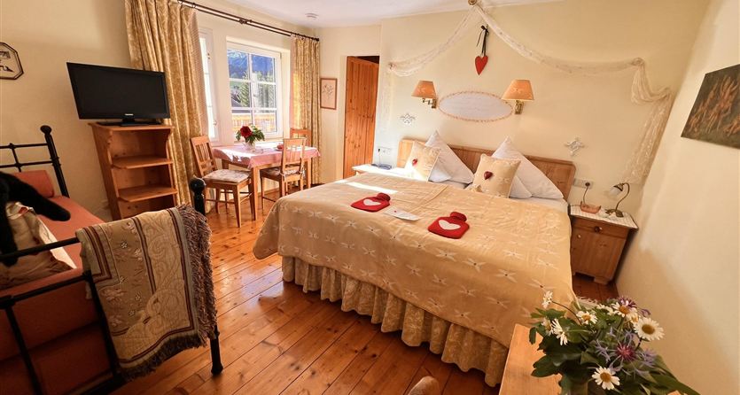 Apartment for 1 to 2 people at Hannas Alpengruss in Seefeld,  
A cozy bedroom with a large double bed and bright curtains.  
In the room, there is a small dining area and a beautiful bouquet of flowers on the table.