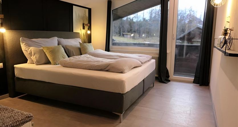 Ein modernes Schlafzimmer mit einem großen Doppelbett und sanfter Beleuchtung. Das Fenster bietet einen Blick auf die Natur.