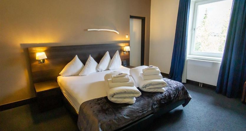 A modern hotel room with a large bed and white pillows.  
The room has a cozy feel with dark walls and blue curtains.