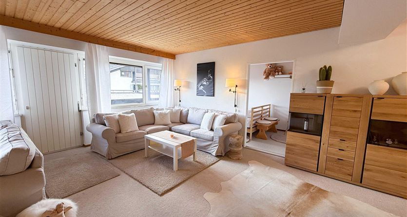 Een lichte woonkamer met comfortabele banken en een houten tafel. Grote ramen zorgen voor veel daglicht en een uitnodigende sfeer.