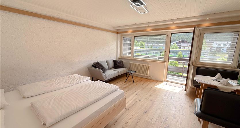 Een heldere en moderne kamer met een tweepersoonsbed en een gezellige bank. Grote ramen bieden uitzicht op de buitenruimte.