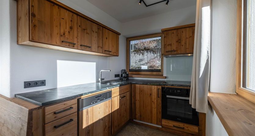 Una cucina moderna in legno con molti armadi e una finestra che garantisce la luce diurna. L'attrezzatura comprende un lavello, un fornello e un forno.