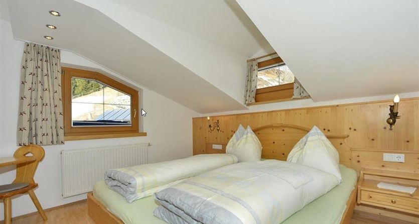 Een gezellige slaapkamer met twee eenpersoonsbedden en een houten wand. Grote ramen laten veel licht binnen en bieden uitzicht naar buiten.