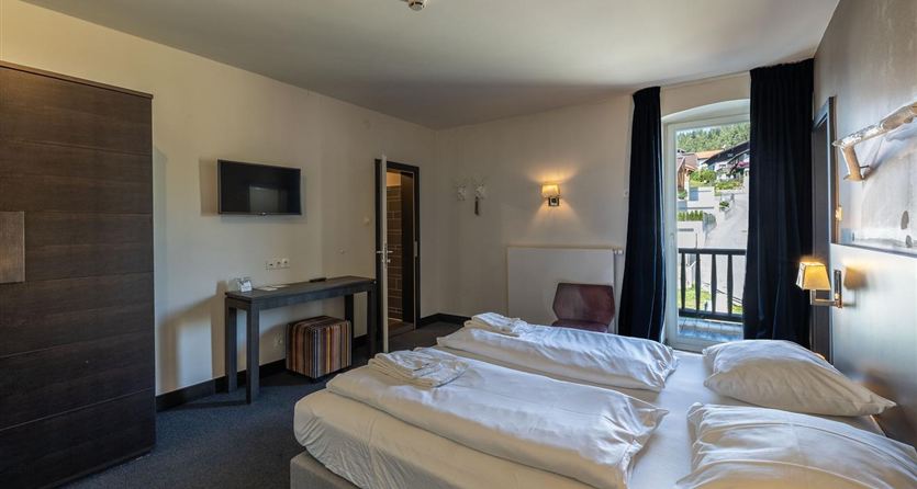 A cozy bedroom with two beds and a large window.  
On the wall, there is a television and a small table.