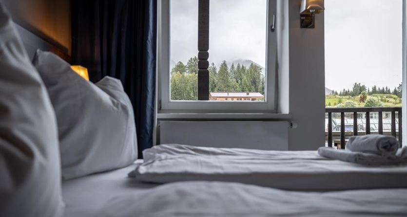 A cozy hotel room with a view of nature. The windows are open and provide a view of a wooded hill.