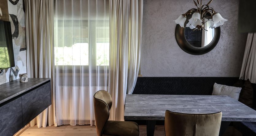 Ein modernes Esszimmer mit einem Holztisch und eleganten Stühlen. Weiche Vorhänge und eine stilvolle Lampe schaffen eine einladende Atmosphäre.