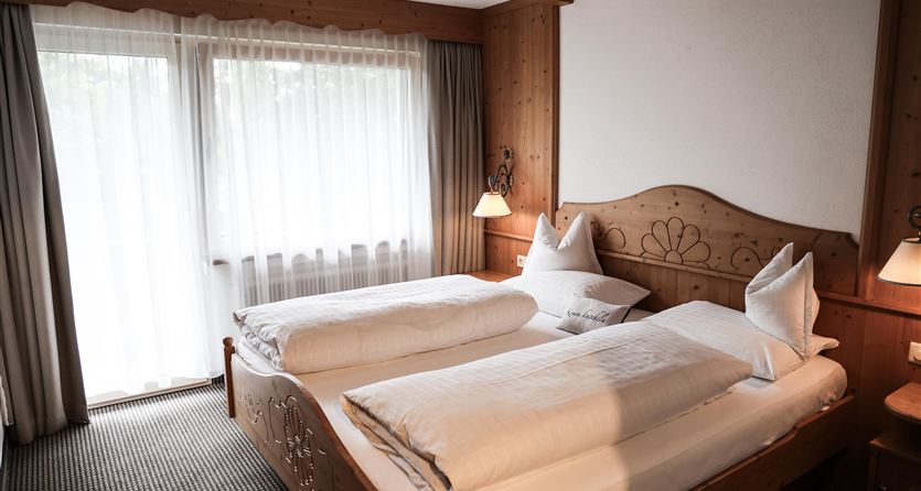 Ein gemütliches Schlafzimmer mit zwei Einzelbetten und Holzdetails. Große Fenster sorgen für viel Tageslicht und eine einladende Atmosphäre.