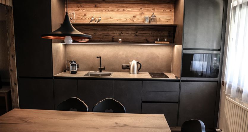 Eine moderne Küche mit dunklen Schränken und Holzregalen. Der Tisch ist aus hellem Holz und es gibt stilvolle Küchenutensilien.