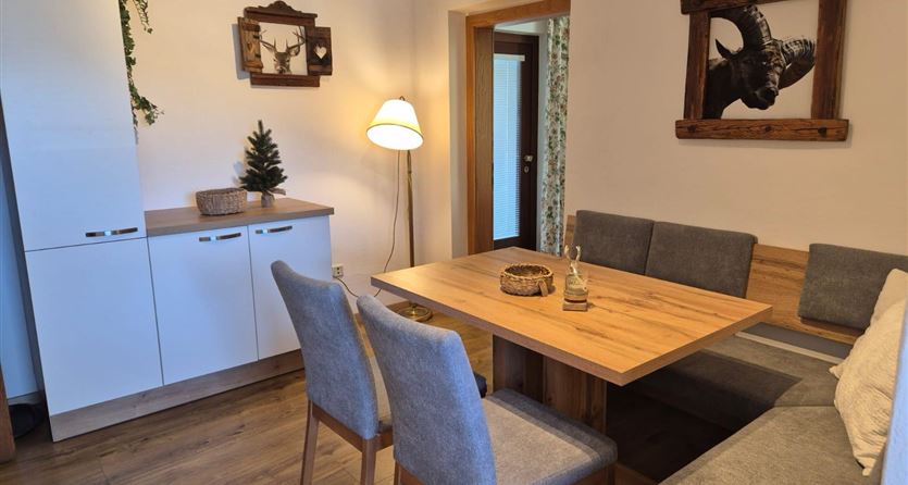 Ein gemütlicher Essbereich mit einem holzfarbenen Tisch und grauen Stühlen. Die Wände sind dekoriert mit Bildern und einer Pflanze steht in der Ecke.