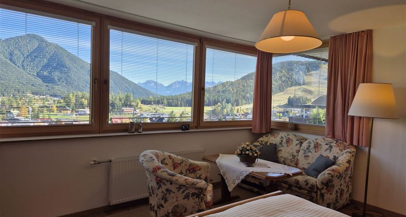 Ein gemütliches Zimmer mit Blick auf die Berge. Die großen Fenster lassen viel Tageslicht herein und bieten eine schöne Aussicht auf die Landschaft.