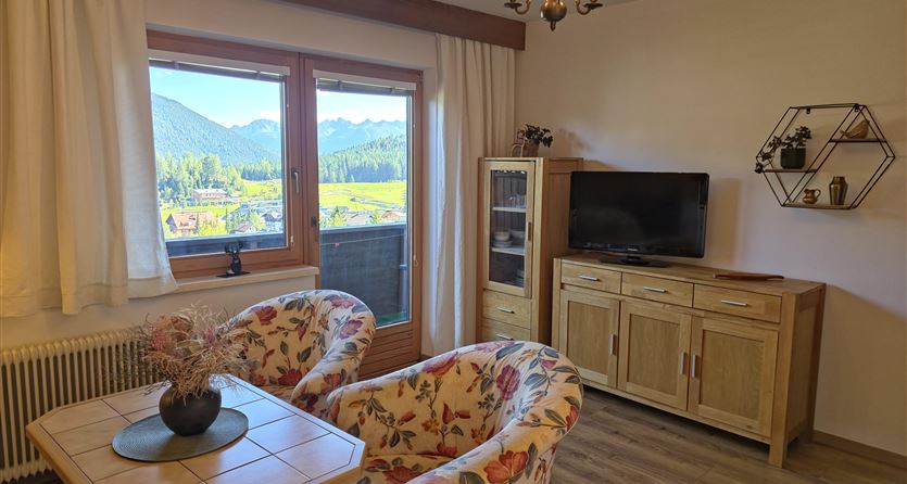 Ein gemütlicher Wohnraum mit floralem Mobiliar und einem Blick auf die Berge. Das Zimmer verfügt über eine hölzerne Kommode und einen Fernseher.