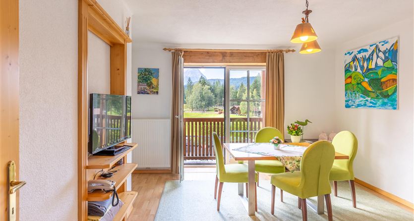 Ein gemütlicher Wohnraum mit einem Essbereich und modernen Möbeln. Große Fenster bieten einen Blick auf die umliegende Landschaft.