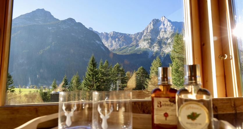 Een uitzicht op indrukwekkende bergen en weelderige bossen. Op de voorgrond staan glazen en flessen op een dienblad.