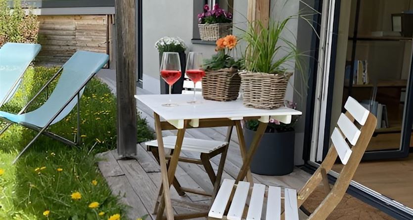 Een gezellige buitenruimte met een kleine tafel en twee stoelen. Op de tafel staan bloempotten en glazen met drankjes middenin een groene weide.