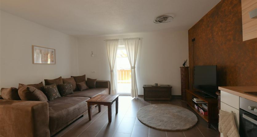 Eine gemütliche Wohnzimmer mit einem beigen Sofa und einem Holztisch. Große Fenster mit Vorhängen lassen viel Licht herein.