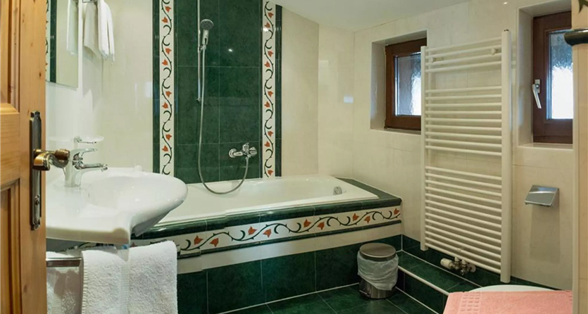 Ein elegantes Badezimmer mit einer Badewanne und einer separaten Dusche. Die Wände sind in grünen und weißen Fliesen gestaltet, ergänzt durch Holzdetails.