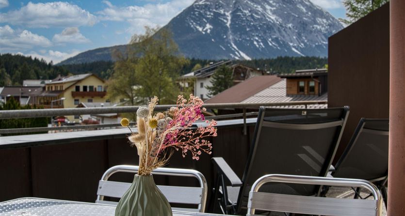 Una terrazza accogliente con un tavolo e un arrangiamento floreale. Sullo sfondo si erge una montagna imponente sotto un cielo sereno.