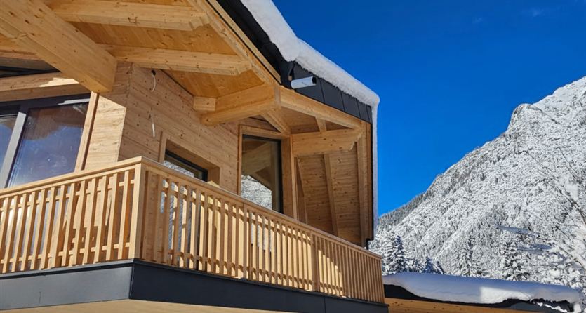 Ein modernes Holzhaus mit einem Balkon, umgeben von schneebedeckten Bergen. Der klare blaue Himmel schafft eine angenehme Atmosphäre.