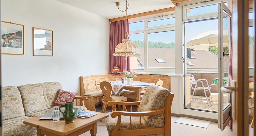 Een lichte woonkamer met gezellige meubels en een tafel. Grote ramen bieden uitzicht op het balkon.