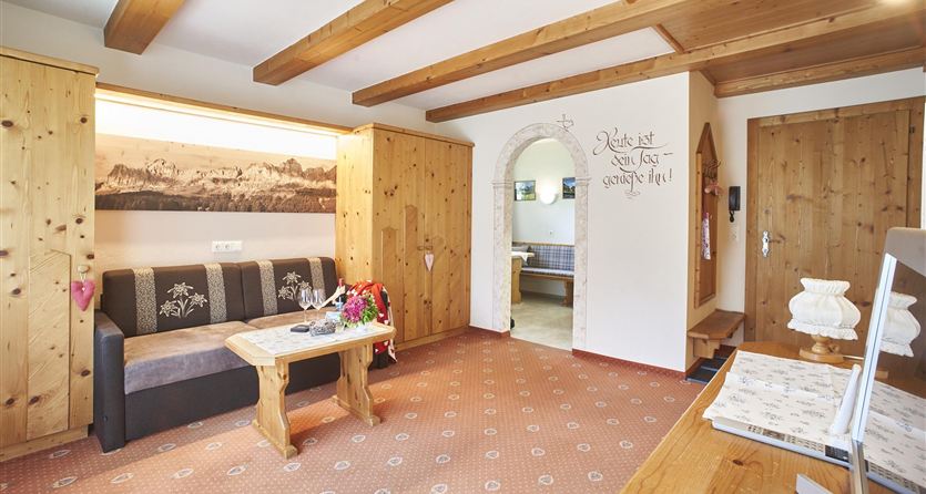 Un accogliente soggiorno con rivestimenti in legno e un divano. La stanza è invitante e luminosa, con belle decorazioni e un passaggio aperto verso la cucina.