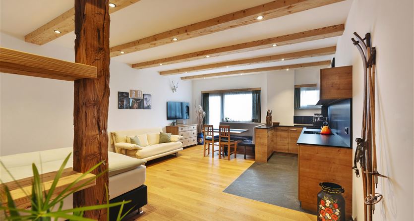 Een moderne woonkamer met houten plafonbalken en een open keuken. De inrichting is gezellig en uitnodigend met een lichte, vriendelijke sfeer.