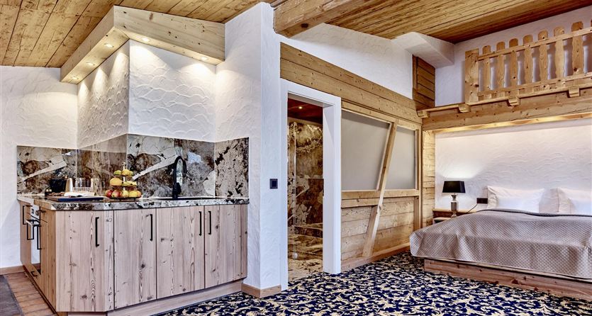 Una stanza accogliente con soffitto in legno e un angolo cottura. La stanza è arredata con un tappeto colorato e un letto a castello.