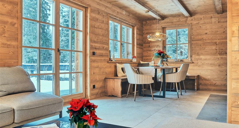 Ein gemütlicher Wohnbereich mit Holzverkleidung und großen Fenstern. Ein Tisch mit Stühlen und einen blühenden Weihnachtsstern auf dem Tisch.