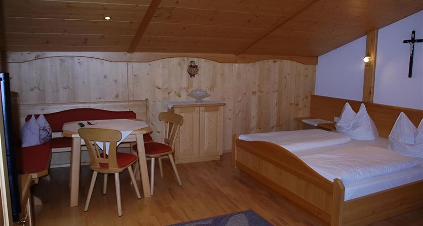 Een gezellige kamer met houten panelen, een eettafel en twee bedden. Aan de muur hangt een kruis, en de inrichting is eenvoudig en uitnodigend.