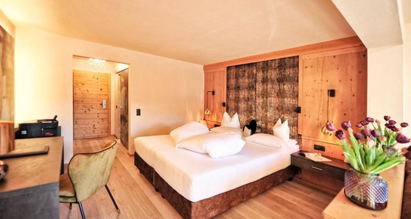 Ein modernes Hotelzimmer mit einem großen Bett und gemütlicher Atmosphäre. Es gibt Holzdekor und eine kleine Sitzecke mit einem Stuhl.