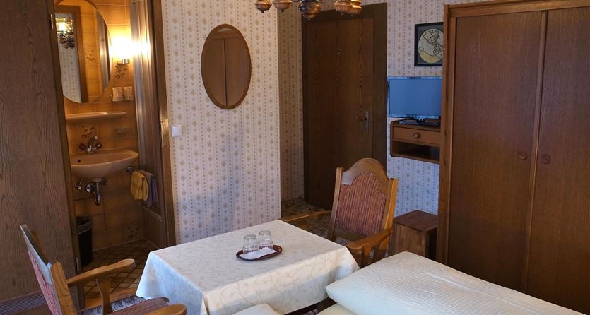 A cozy room with wooden furniture, a table, and two beds. A lamp and a mirror hang on the wall.