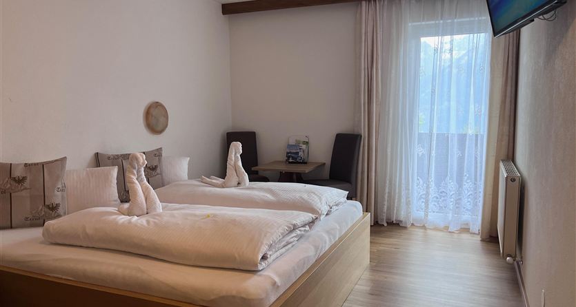 Een gezellige slaapkamer met een tweepersoonsbed en twee handdoeken die als zwanen gevouwen zijn. Naast het bed staat een tafel en een televisie aan de wand.