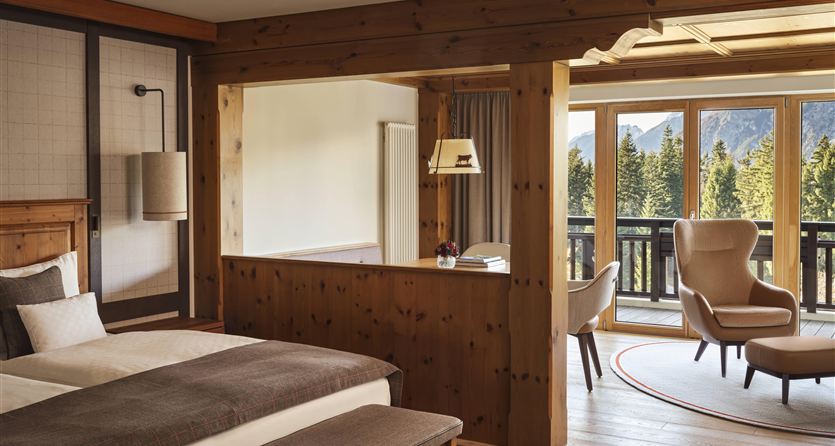 Ein modernes Zimmer aus Holz mit einem großen Fenster, das einen Blick auf die Natur bietet. Es gibt ein bequemes Bett und einen gemütlichen Sitzbereich.