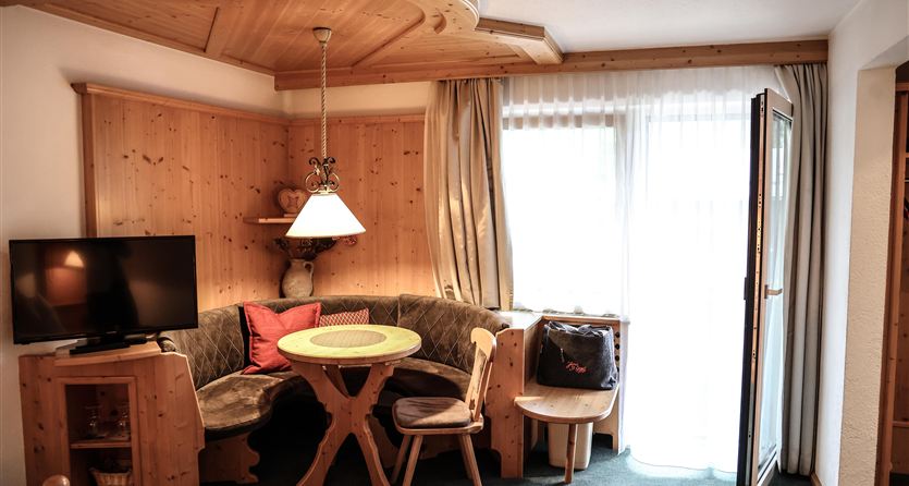 Ein gemütlicher Wohnbereich mit holzgetäfelten Wänden und einem runden Tisch. Ein Fenster sorgt für viel Tageslicht und Zugang nach draußen.