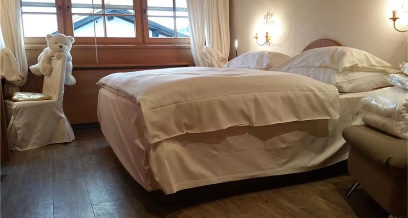 Een gezellige slaapkamer met een groot bed en witte beddengoed. Aan de muur staat een kussen met een pluchen teddybeer.