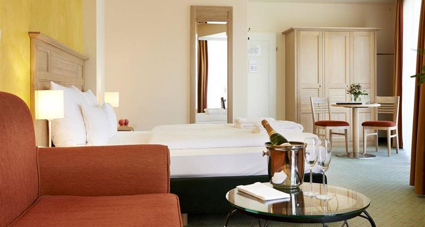 Een moderne hotelkamer met twee bedden en een comfortabele bank. Er is een tafel en stoelen, evenals een decoratief element met een bloem.