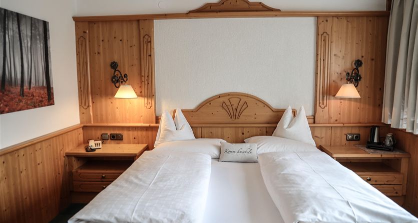 Ein gemütliches Schlafzimmer mit einem großen Doppelbett und hölzernen Wänden. Es gibt eine schöne Wanddekoration und stimmungsvolle Beleuchtung neben dem Bett.