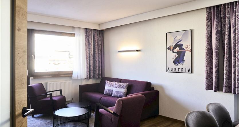 A modern living room with a cozy sofa and two chairs. On the wall hangs a picture with the inscription "Austria".