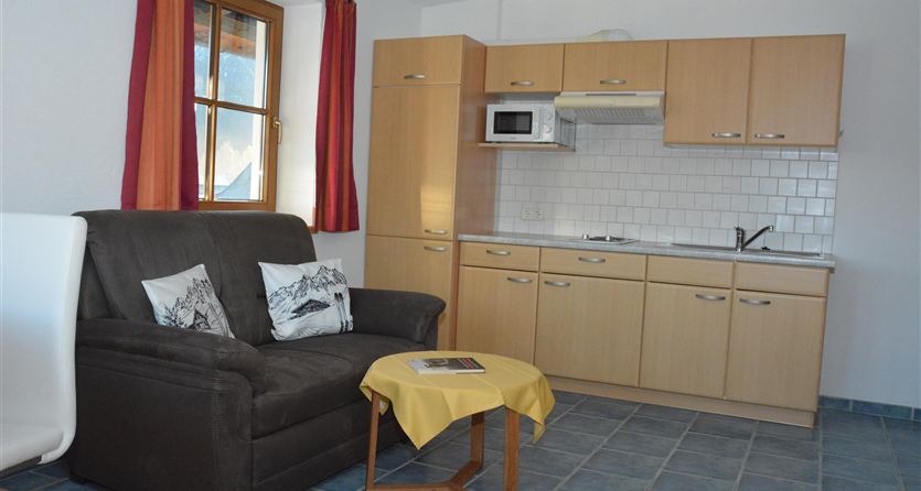 Een gezellige woonkamer met een zwarte bank en een kleine tafel. De moderne keuken is in warme houttinten ingericht en biedt een uitnodigende sfeer.