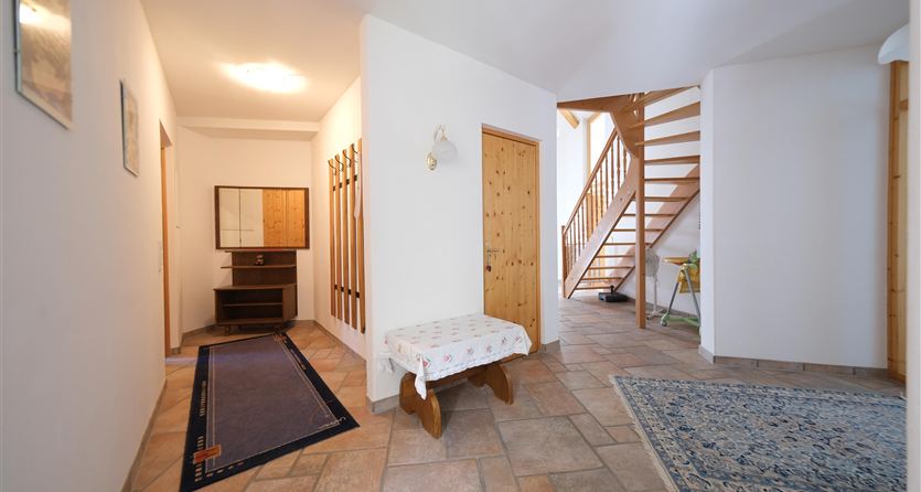 Een lichte gang met een houten tafel en een trap. De vloer is met tegels bedekt en er is een tapijt evenals enkele decoratieve elementen.