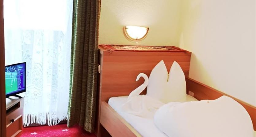 A cozy bedroom with a single bed and decorative cushions in the shape of swans. The room has a television and a window with curtains.