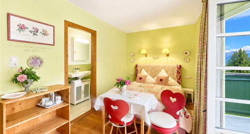A cozy room with a double bed and a dining area. The walls are painted in a soft green shade, and the light is friendly and inviting.