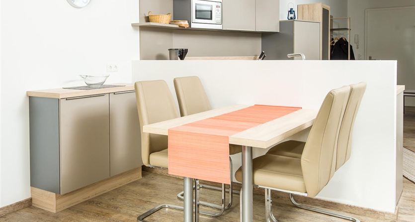 Een moderne keuken met een eetgedeelte. De tafel heeft een oranje tafellaken en de stoelen zijn beige.