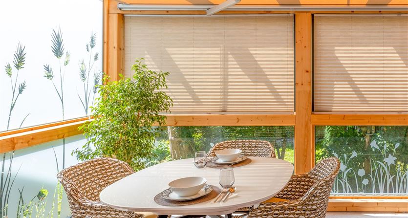 Ein heller, einladender Essbereich mit einem runden Tisch und gemütlichen Stühlen. Große Fenster und Pflanzen schaffen eine angenehme Atmosphäre.