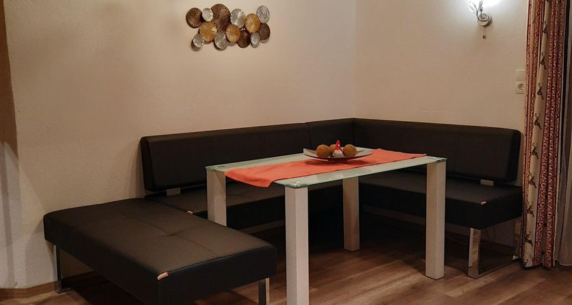 Ein gemütlicher Essbereich mit einer grauen Sitzbank und einem Tisch. Auf dem Tisch steht eine Obstschale und die Wände sind mit Holz verkleidet.