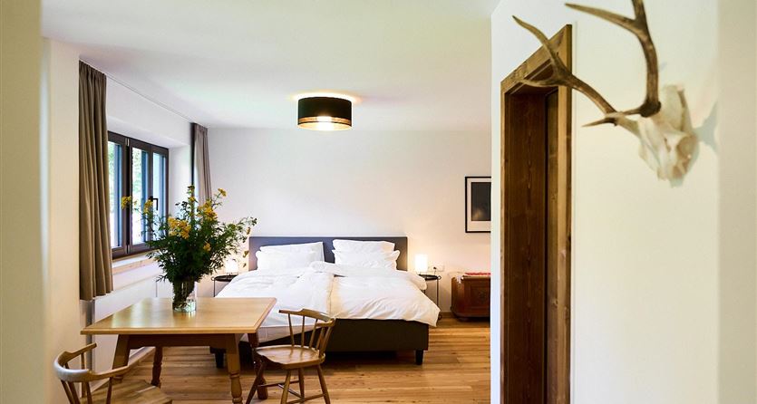 Ein modernes Schlafzimmer mit einem Doppelbett und Holzboden. Ein Tisch mit Stühlen und frischen Blumen verleiht dem Raum eine gemütliche Atmosphäre.