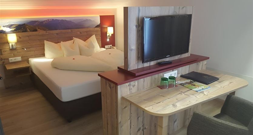 Ein gemütliches Hotelzimmer mit einem großen Bett und modernem Holzdekor. Der Raum ist hell und einladend, ausgestattet mit einem Fernseher und einem kleinen Arbeitsplatz.