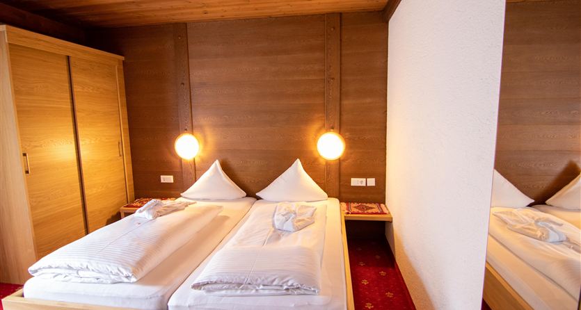 Een gezellige slaapkamer met twee bedden, houten wandbekleding en warm licht. De ruimte heeft een uitnodigende sfeer en is goed uitgerust.