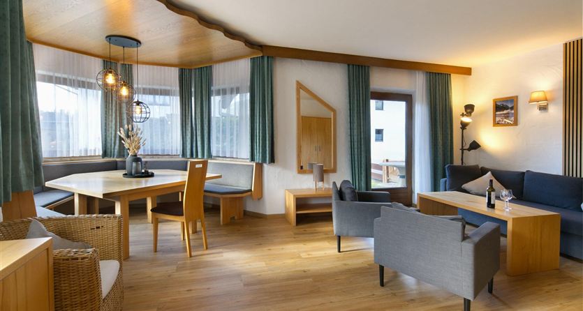 A modern living room with bright wood finishes and large windows. There are cozy seating options and a dining table in an inviting atmosphere.